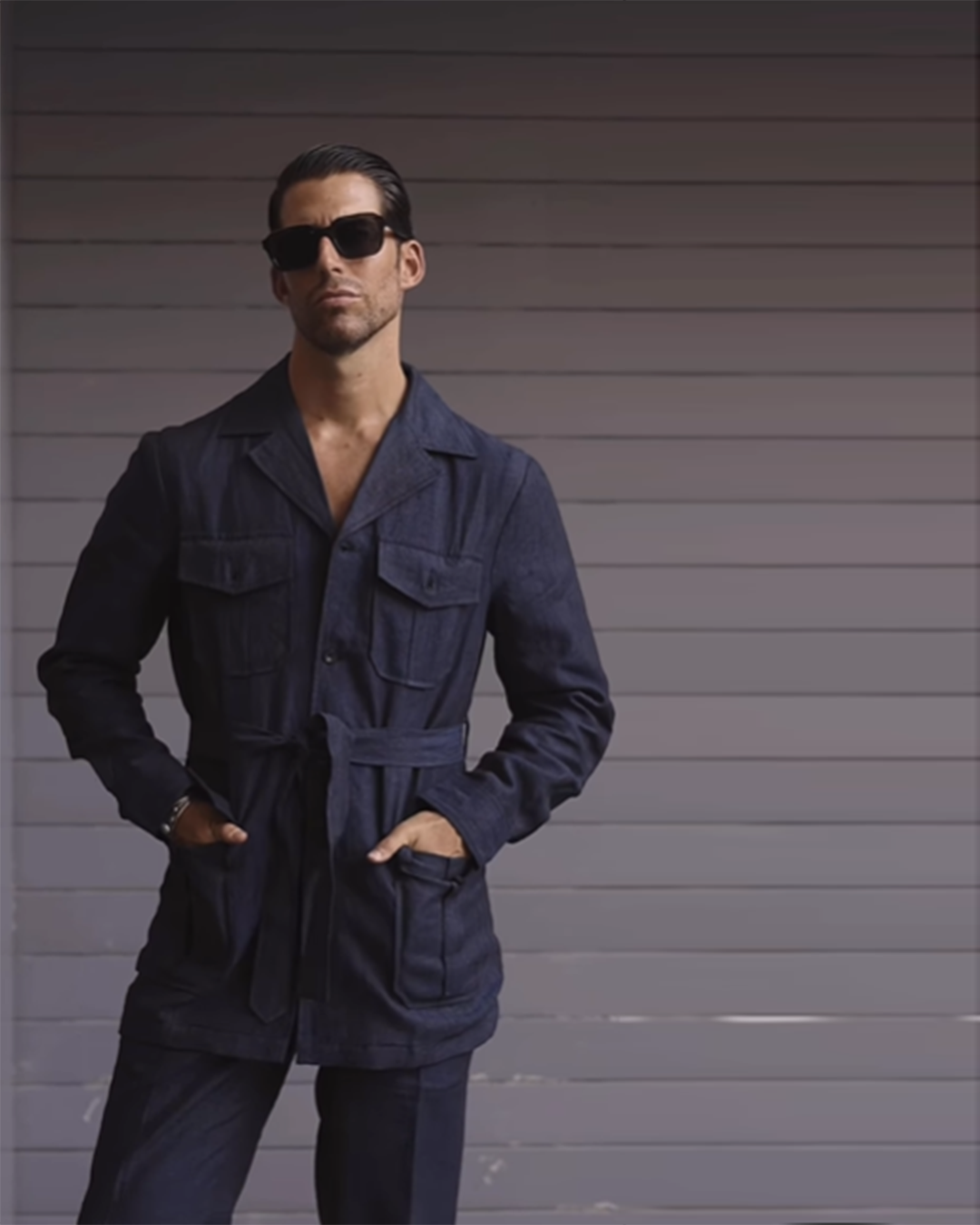 Model wearing the safari jacket in linen for men by Luxire in dark indigo hands in pockets wearing sunglasses