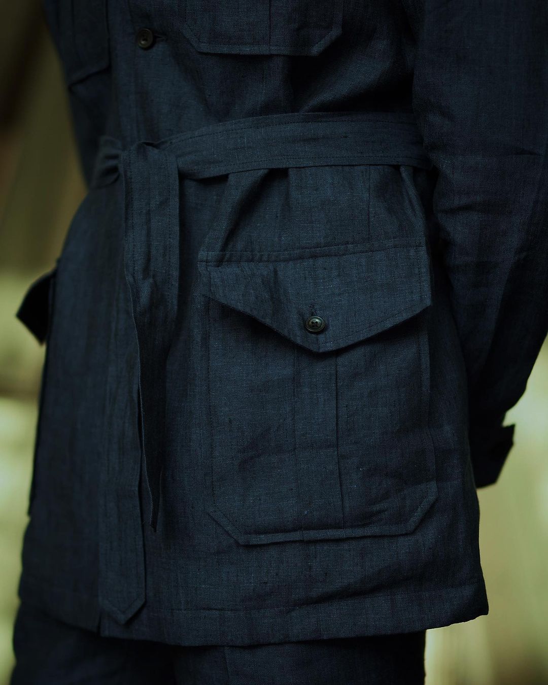 Close up of model wearing the safari jacket in linen for men by Luxire in dark indigo hands behind back